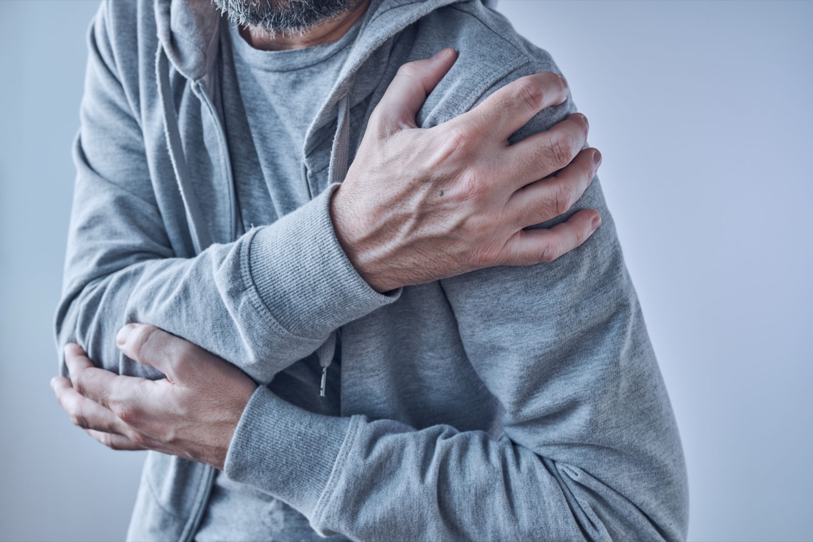 Man in grey hoodie clutching his shoulder in pain