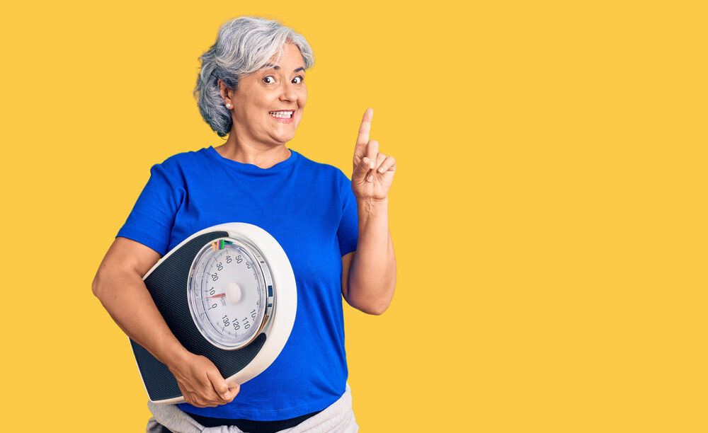Diet and weight loss concept. Happy young woman with floor scale on pink background